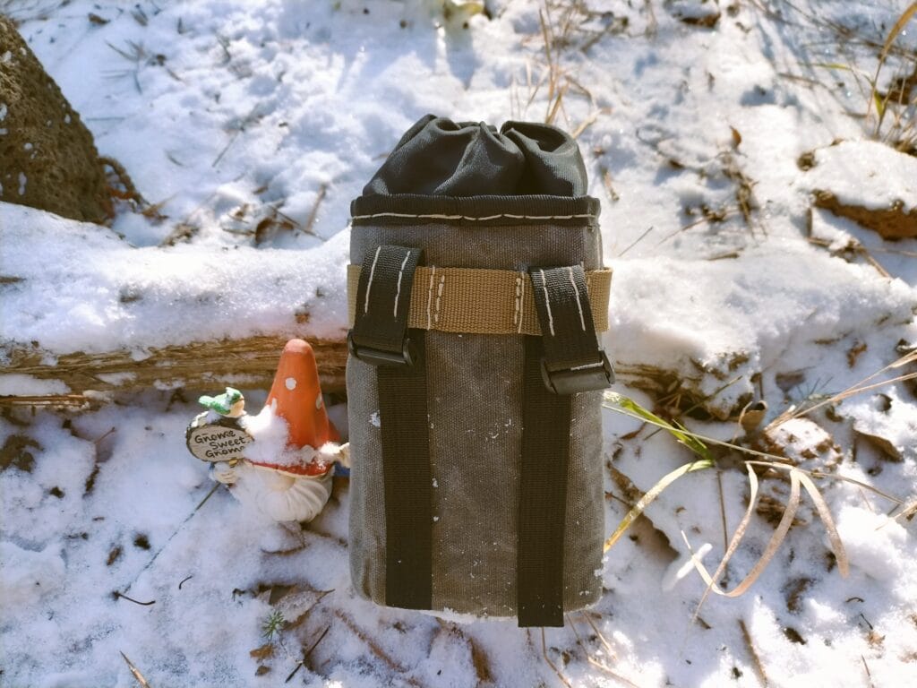 Front view of a DIY bike stem bag with two straps next to a gnome in a snowy garden.