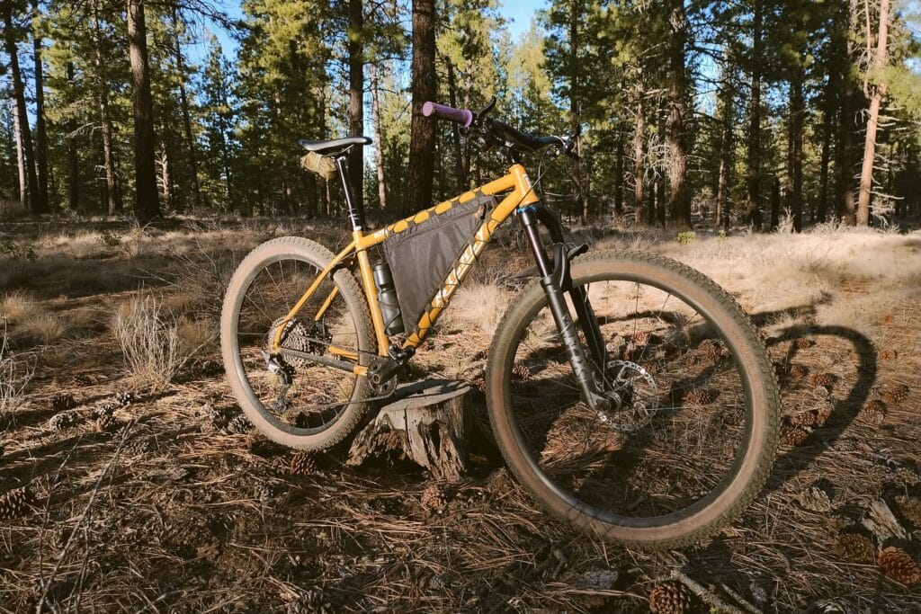 Front profile view of a yellow mountain bike in a low light pine forest.