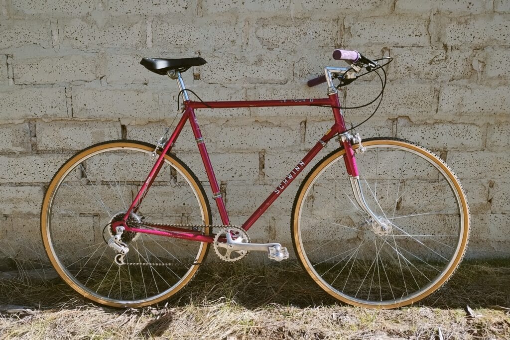 1977 Schwinn Le Tour II converted to 1x flat bar setup and gravel tires leaned against an old brick wall.