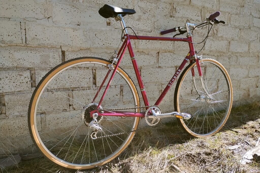 1977 Schwinn Le Tour II converted to 1x flat bar setup and gravel tires leaned against an old brick wall.