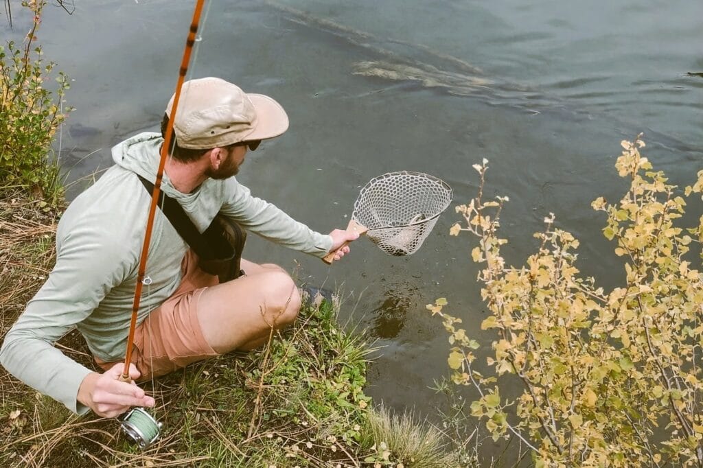 A man landing a trout in Handy Pak Net in one hand and a fly rod in another hand.