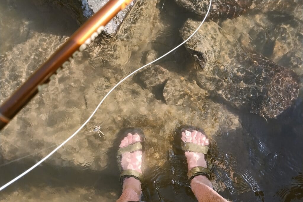 Two feet in sandals in a rocky riverbed.