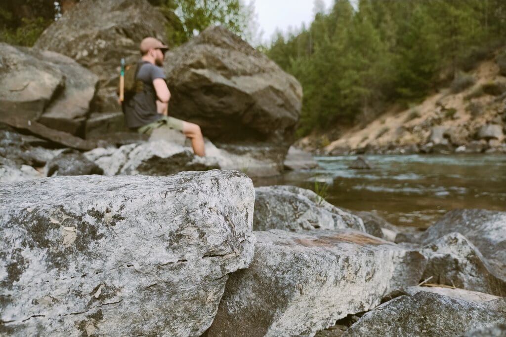 A man sitting on a rock at a riverbank.